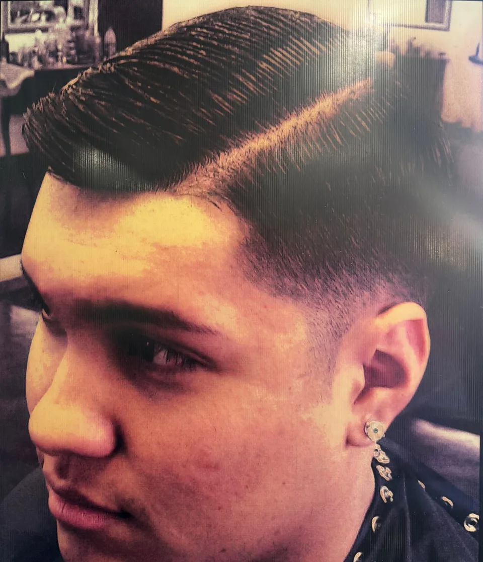 A slicked-back cut with a hard part and a low fade